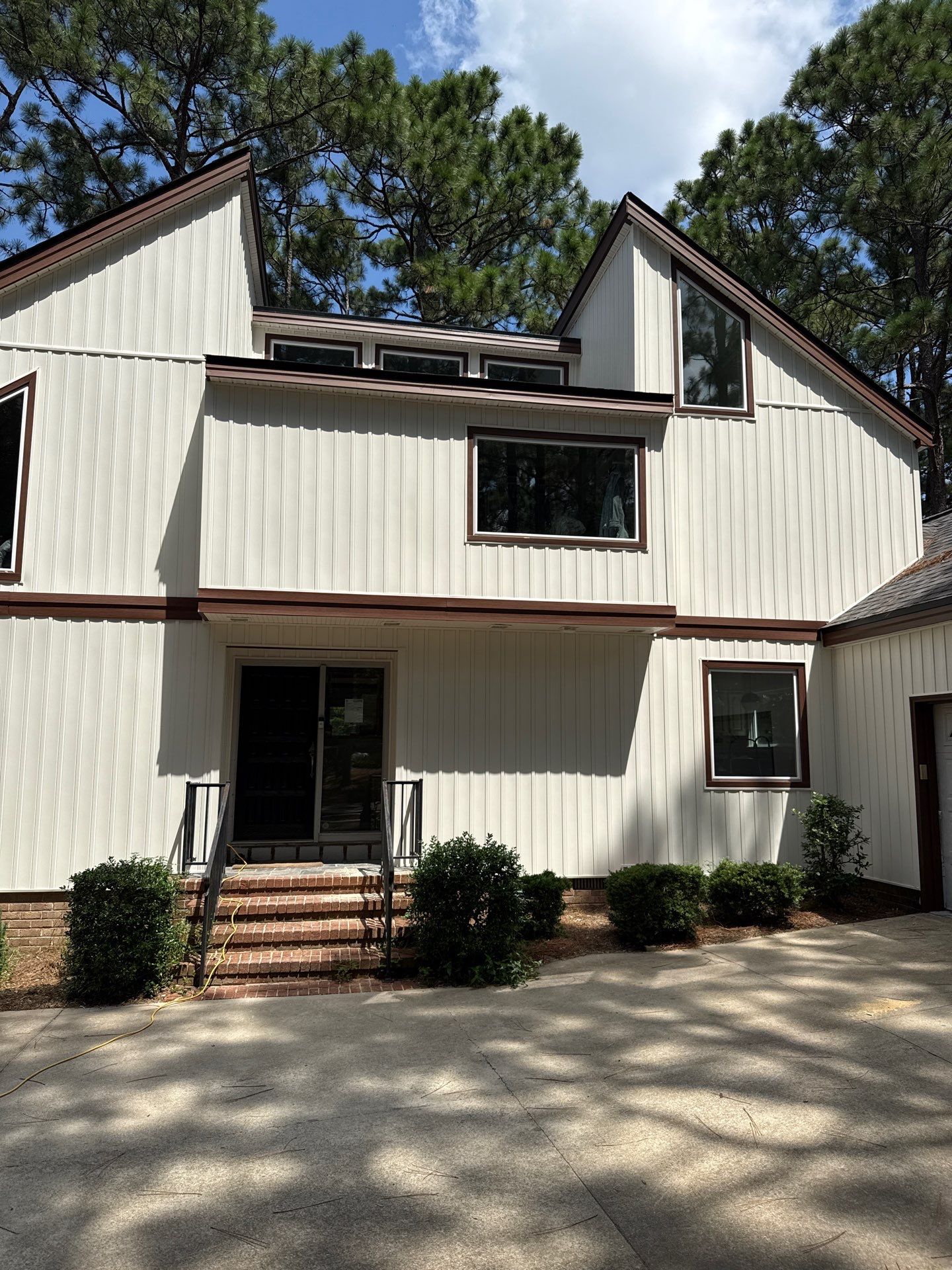 Modern home exterior with new windows, showcasing improved curb appeal and energy efficiency, surrounded by greenery and a clear blue sky.