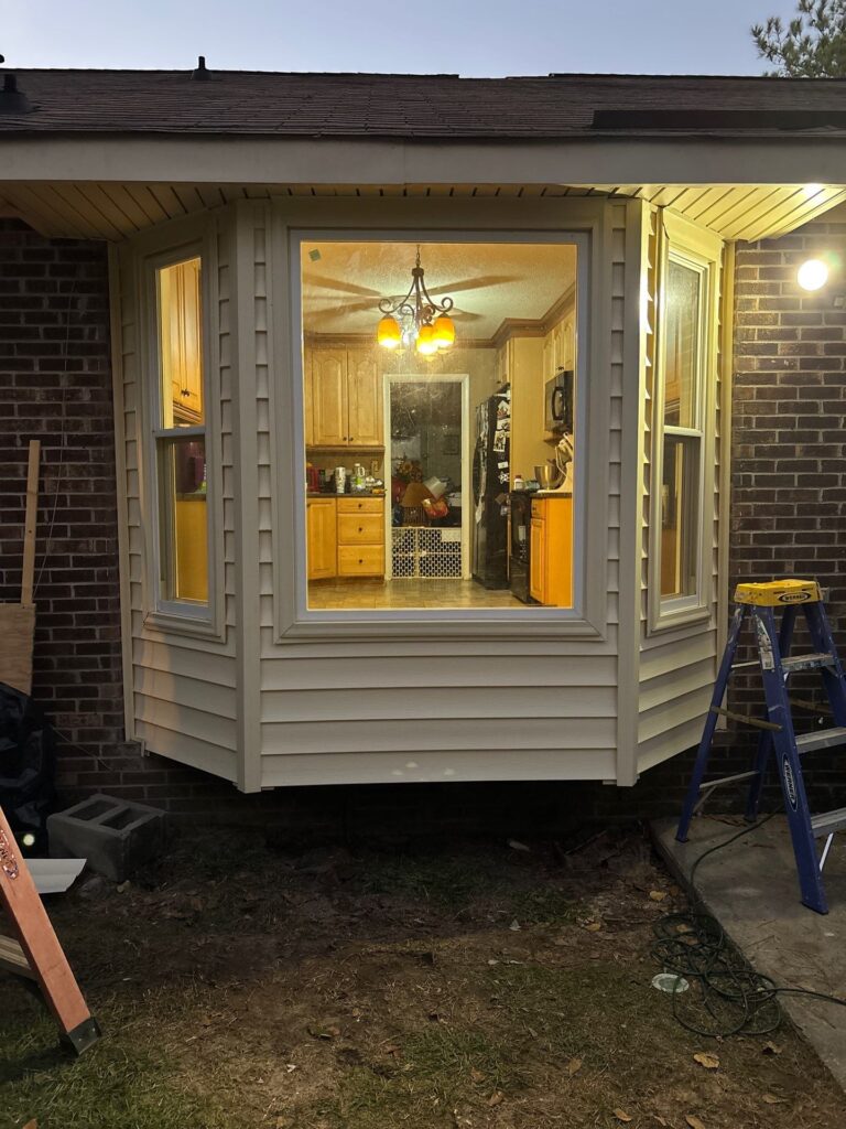Newly installed bay window showcasing modern design, enhancing home aesthetic, with illuminated kitchen interior visible through glass, emphasizing energy efficiency and curb appeal.